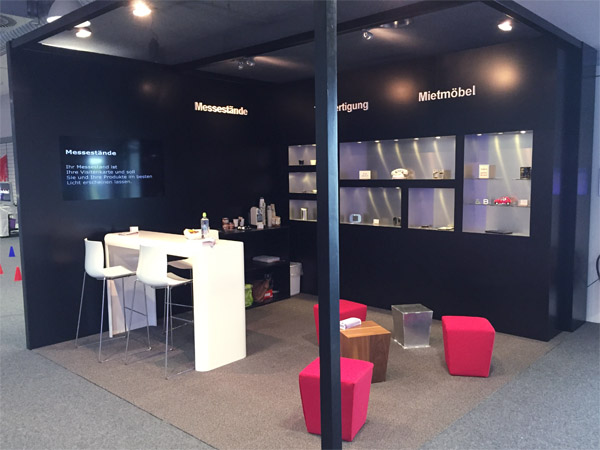 Messestand mit Einbauregalen, Br�ckentisch, Loungehocker, Beleuchtung
gefr�sten Logos und eingebautem Display